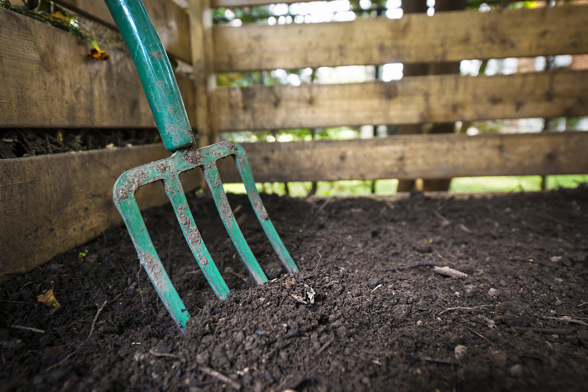 Garden fork turning compost. Garden fork turning black composted soil in wooden compost bin