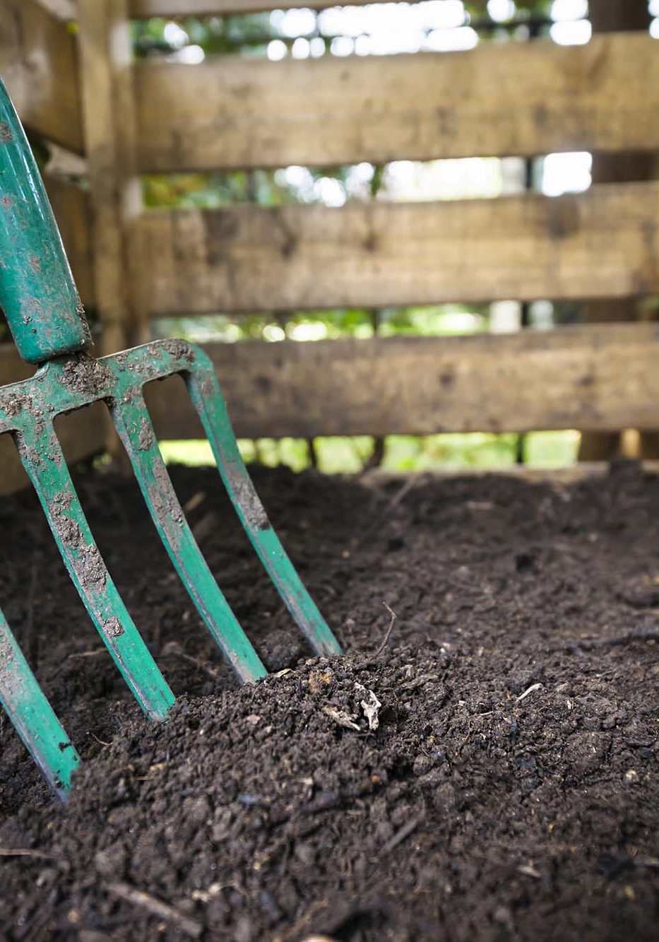Garden fork turning compost. Garden fork turning black composted soil in wooden compost bin